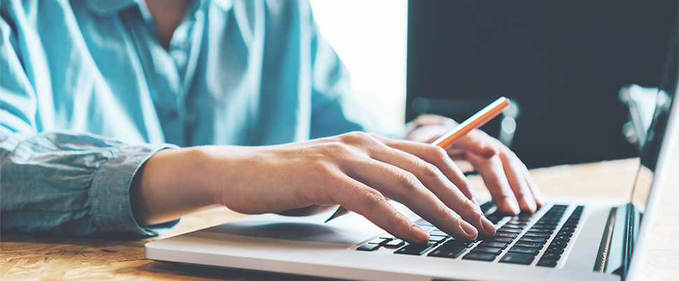 Person sitting at table typing on a laptop keyboard.